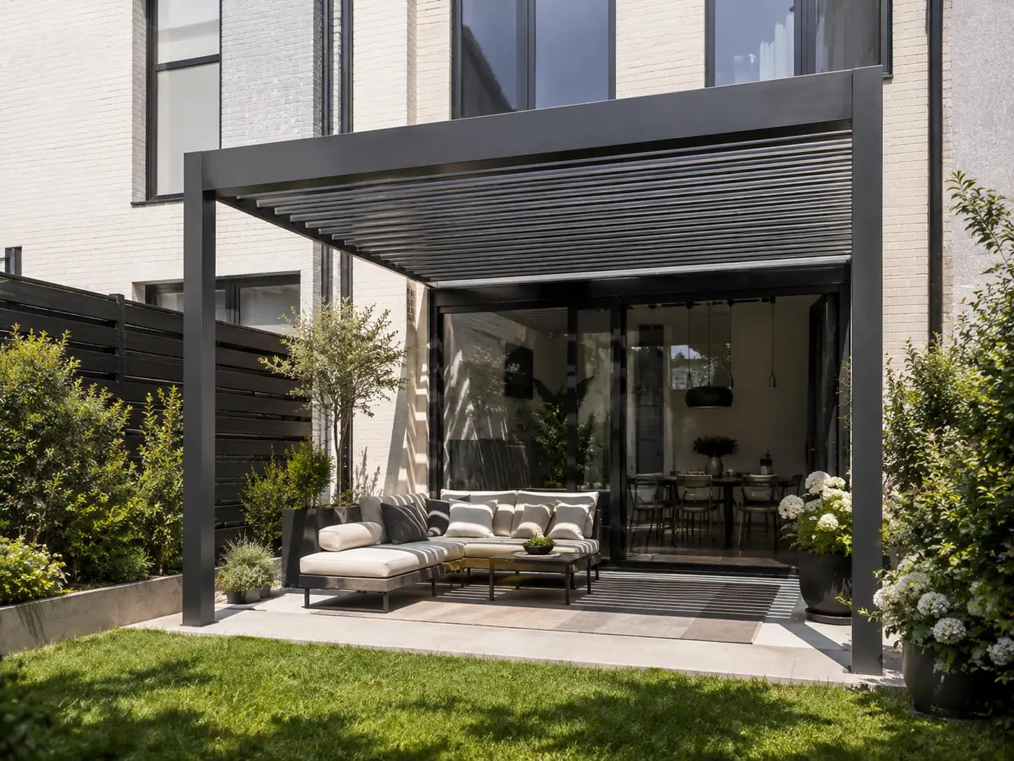 Czarna pergola bioklimatyczna z lamelami i oświetleniem LED nad tarasem z aneksem grillowym