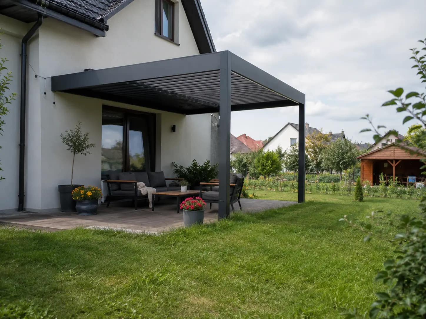 Pergola bioklimatyczna wolnostojąco-przyścienna nad tarasem z meblami ogrodowymi